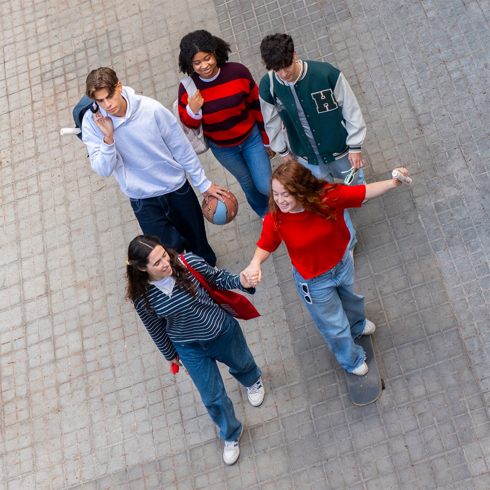 Five young people standing on a sidewalk, interacting with each other.