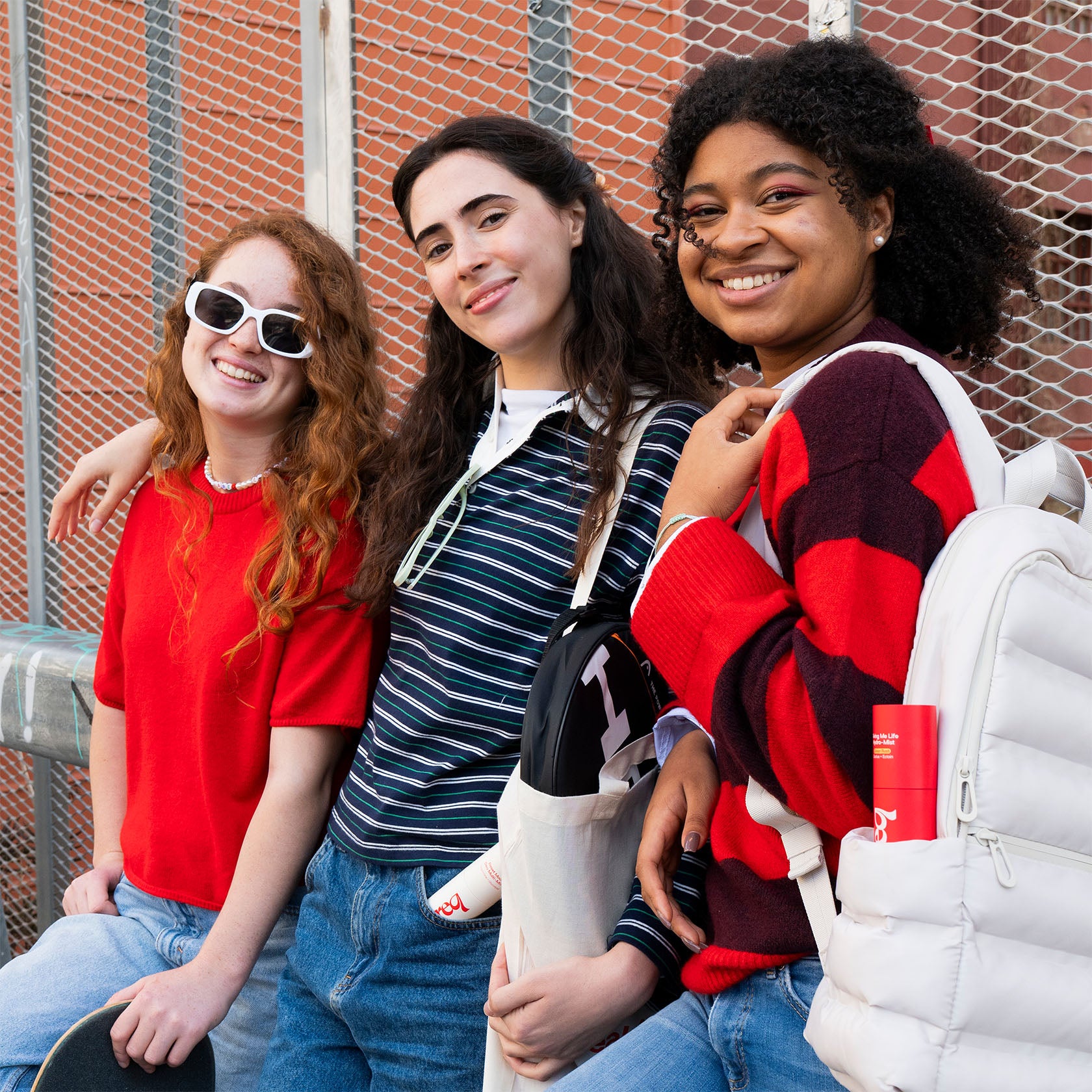 Three young women posing together against a brick wall.