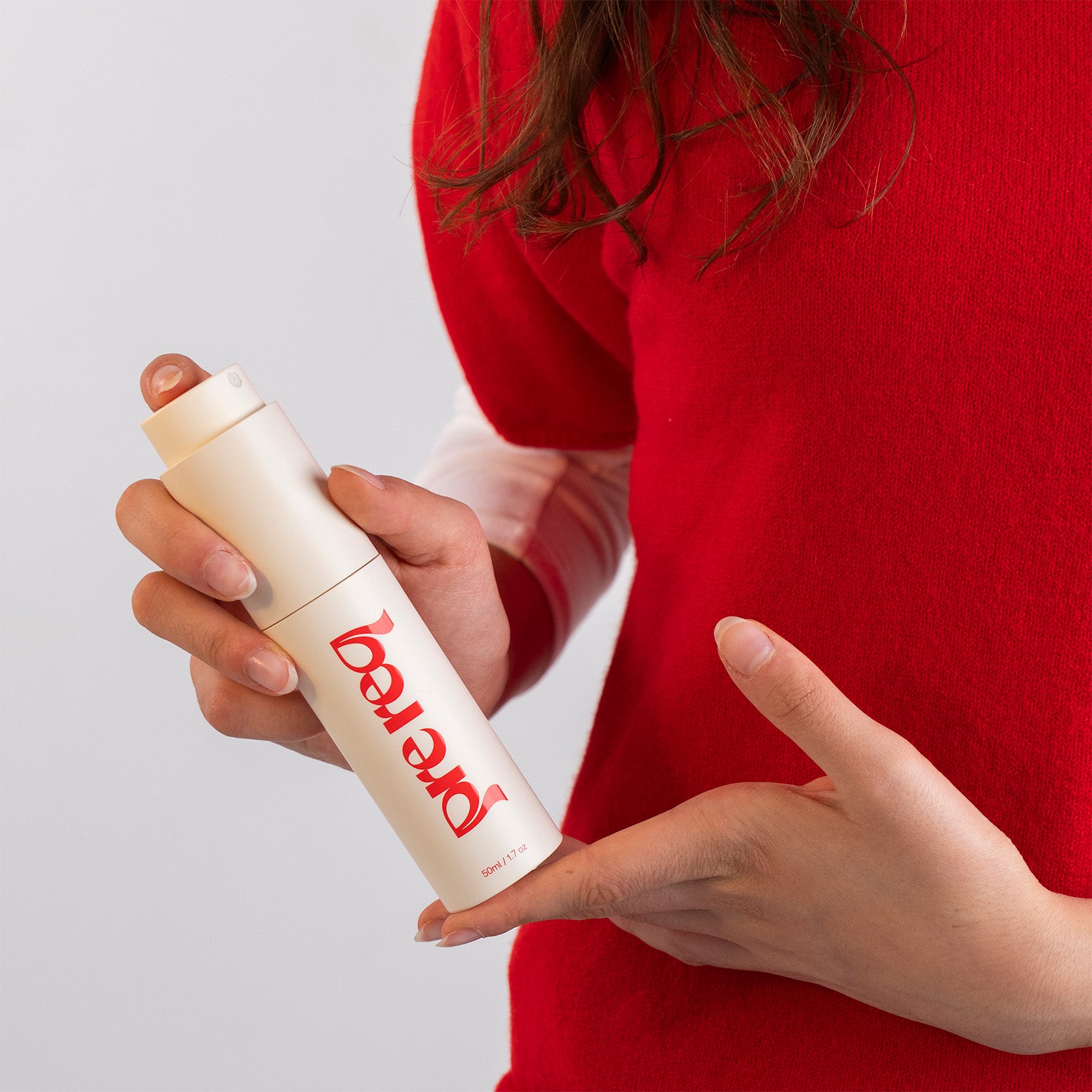 Person holding a white bottle with red branding against a plain background