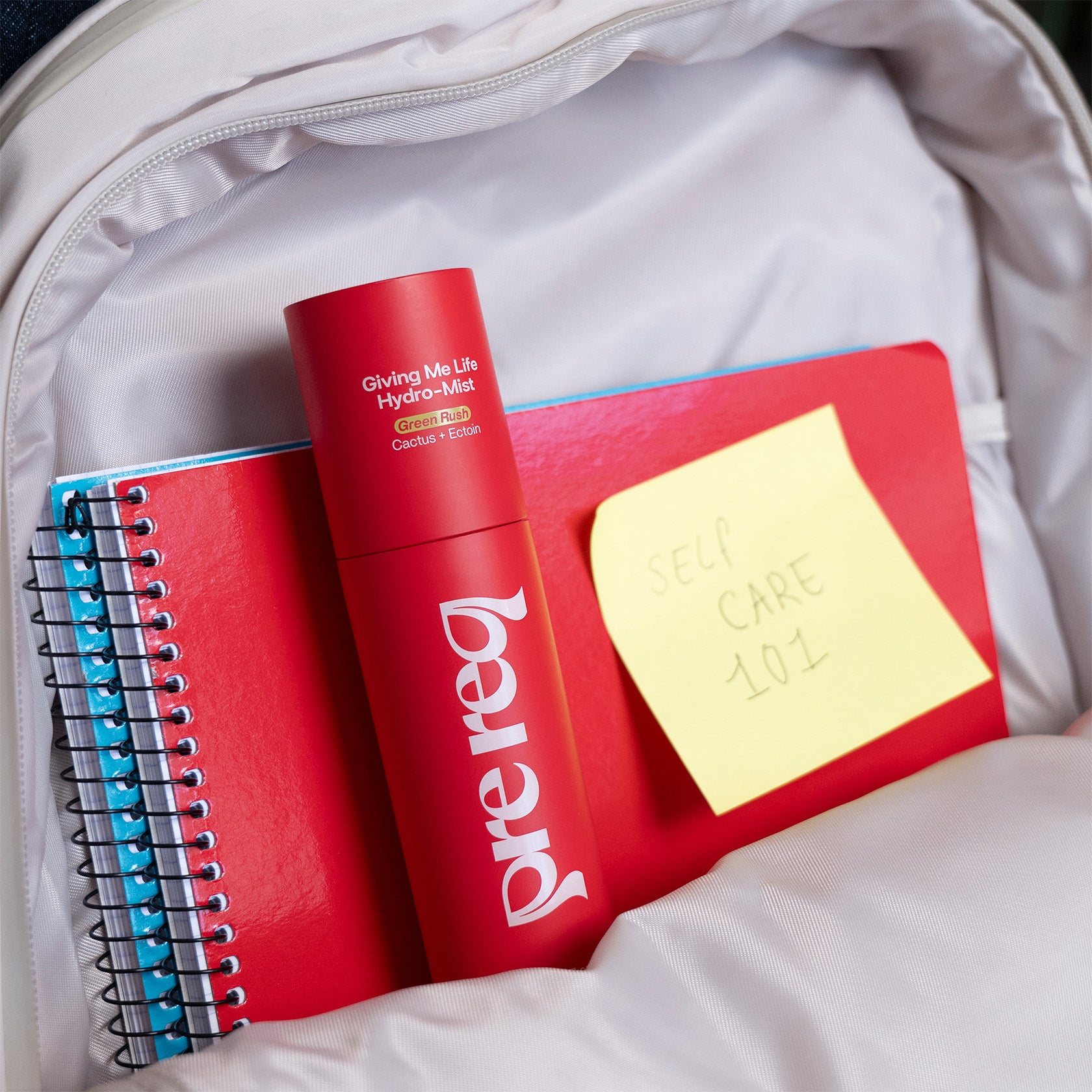 Red bottle with 'prereq' branding, notebooks, and a yellow sticky note inside a backpack.