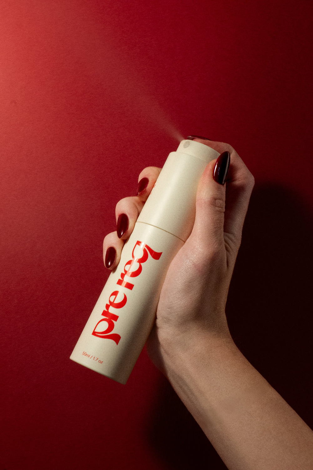 Hand with red nails holding a deo mist spray bottle with red text against a red background